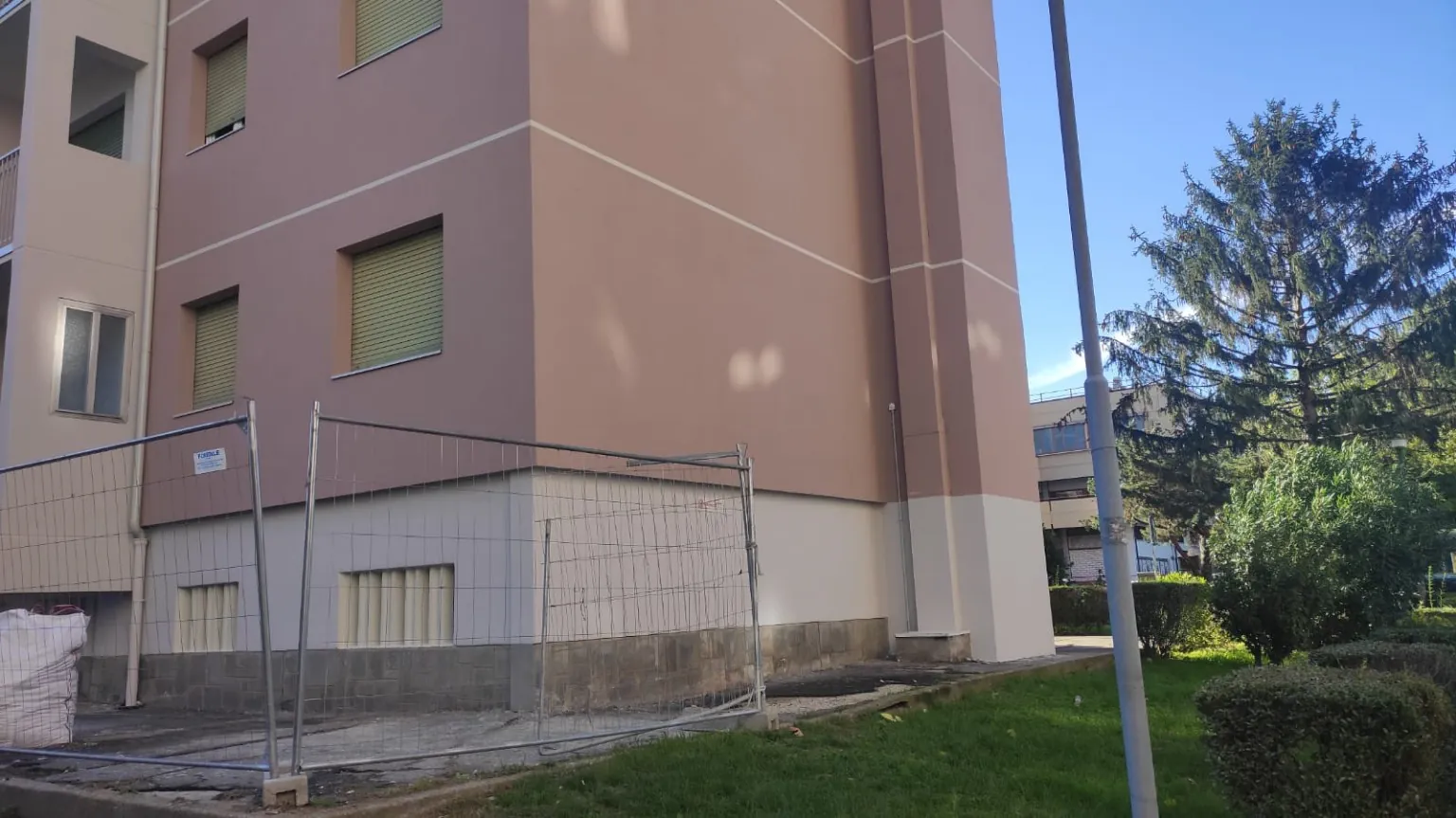 Parte inferiore di una facciata rosa con finestre e area verde